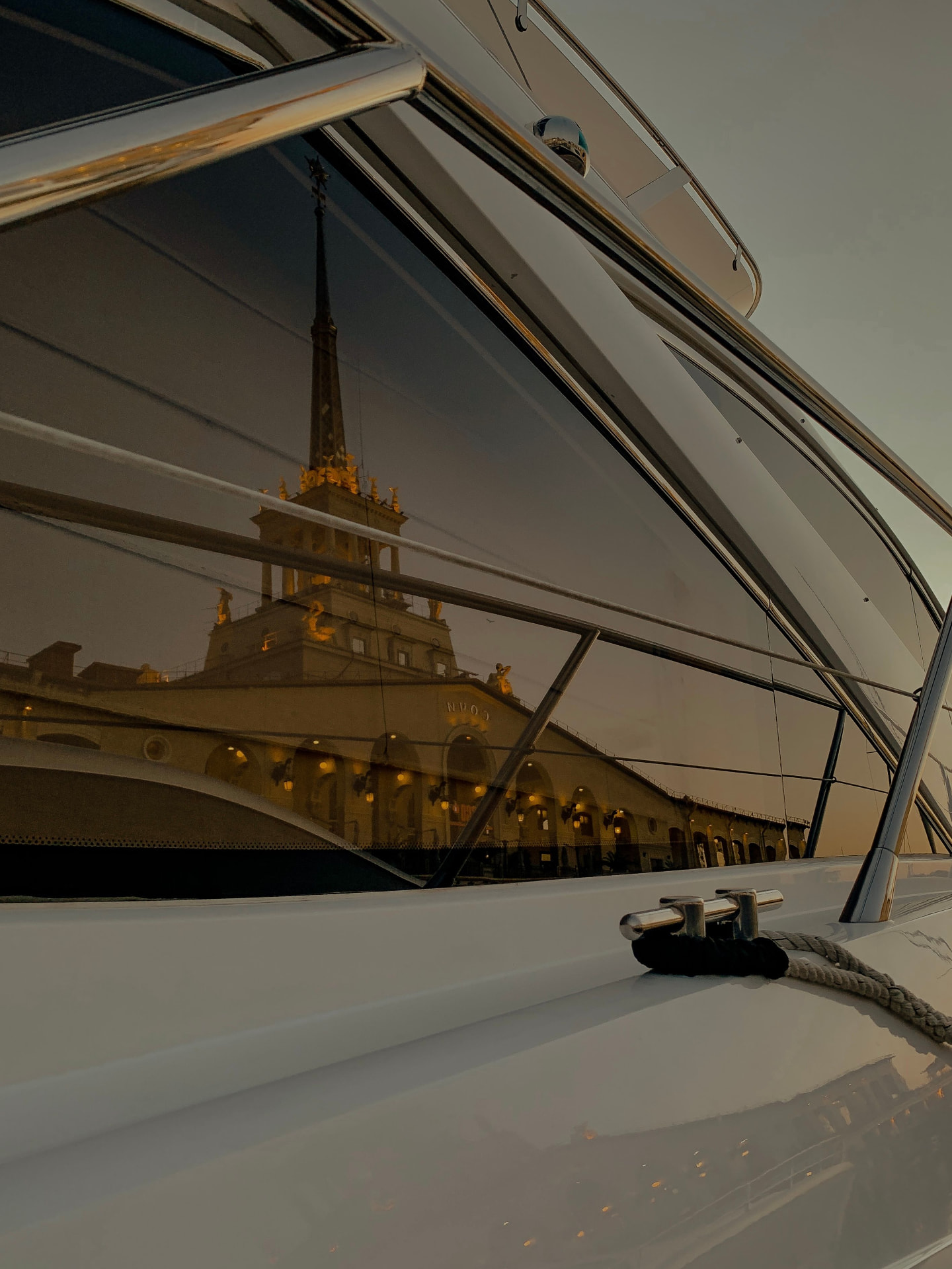 Reflections of an evening harbour town in the dark glass of a superyacht's windows