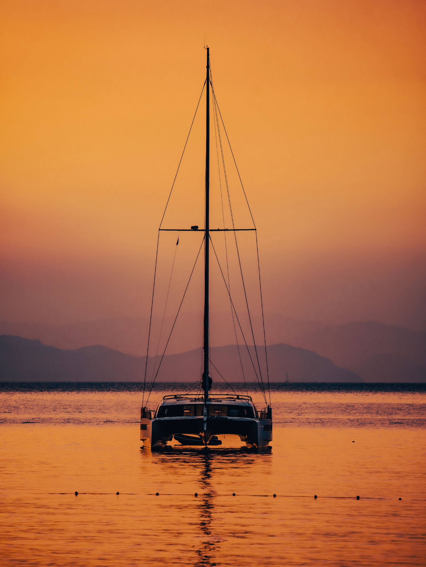 A catamaran at anchor against an amber Mediterranean sunset